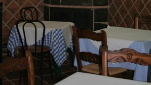 A dining area with tables covered by checkered tablecloths, a stone fireplace, and a wall-mounted deer antler decoration. - Apartamentos Sierra del Hacho (Montejaque)