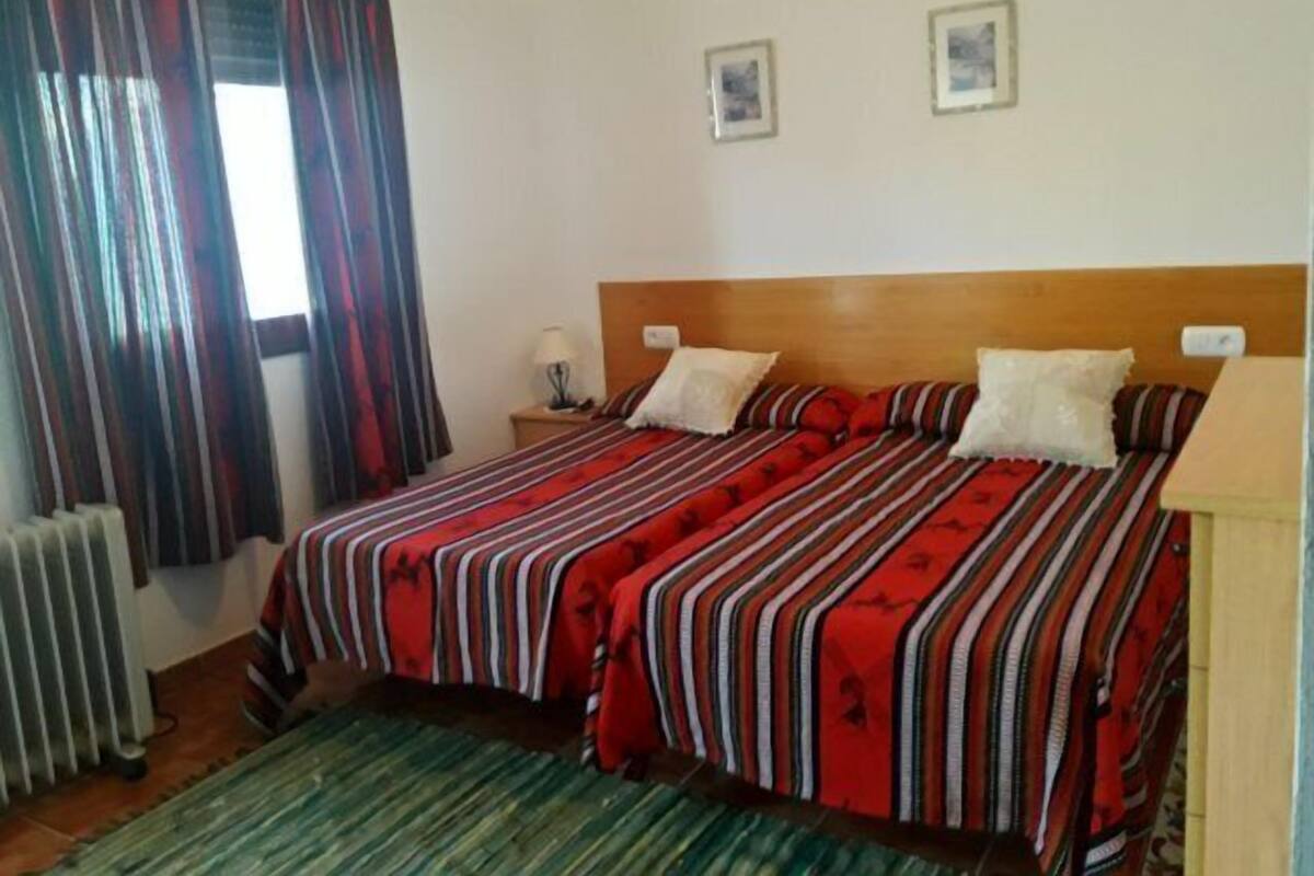 A bedroom with a bed, two pillows, a nightstand with a lamp, and a window with curtains.