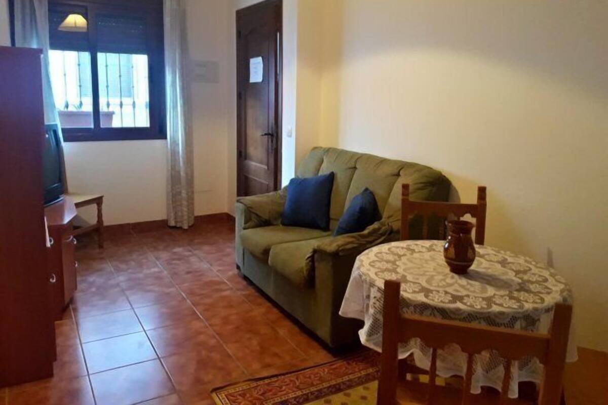 A living room with a sofa, a small table with a lace tablecloth, a television, and a window with curtains.