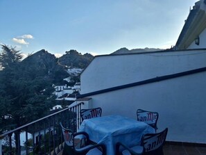 A balcony with a table and chairs, overlooking a mountainous landscape with white buildings. - Apartamentos Sierra del Hacho (Montejaque)