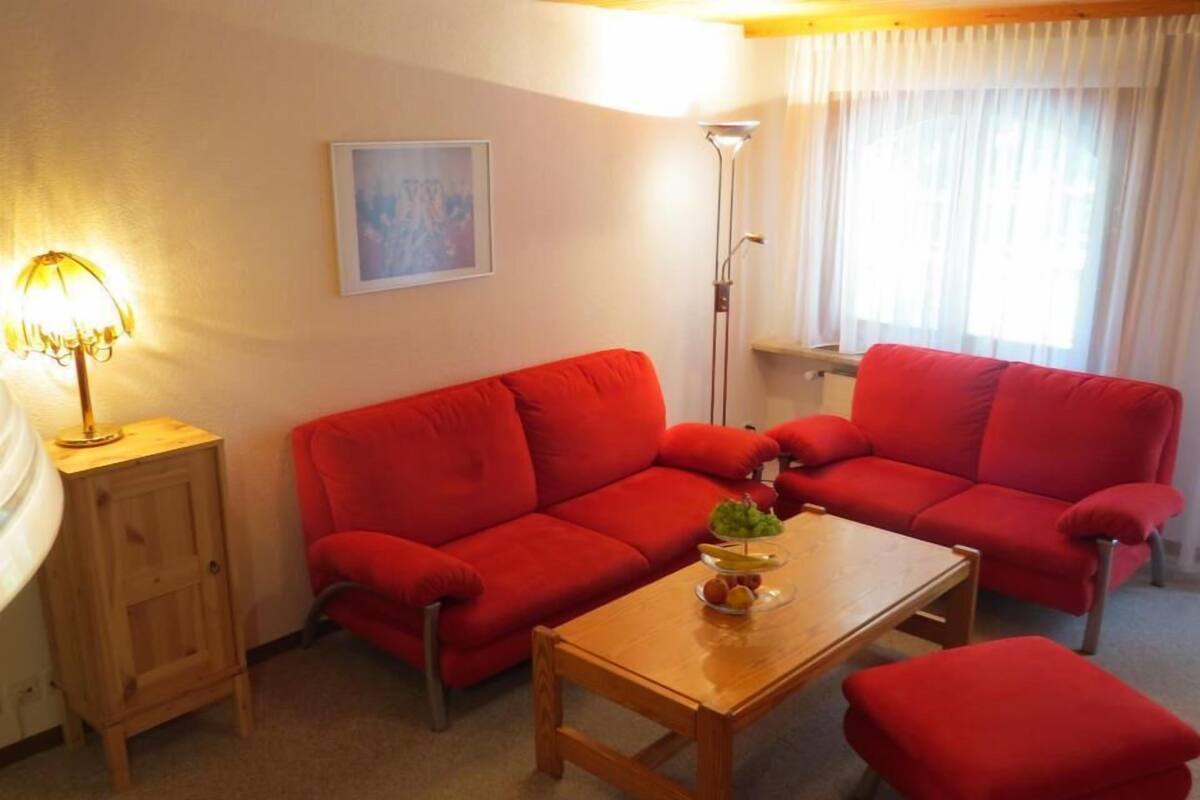 A living room with a red sofa set, a wooden coffee table with fruit, a lamp, and a painting on the wall.