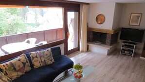 A living room with a blue sofa, a glass coffee table with fruit, a fireplace, and a TV stand.