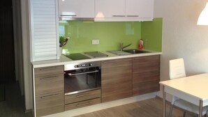 A modern kitchen with white cabinets, a green backsplash, stainless steel appliances, and a white dining table.