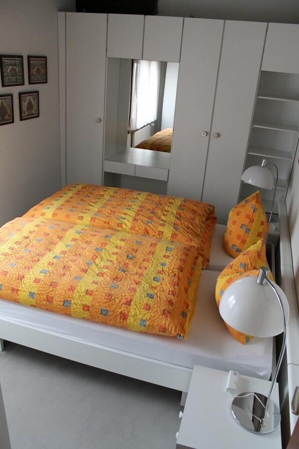 Una cama con un edredón colorido, una lámpara de noche y un armario con espejo.