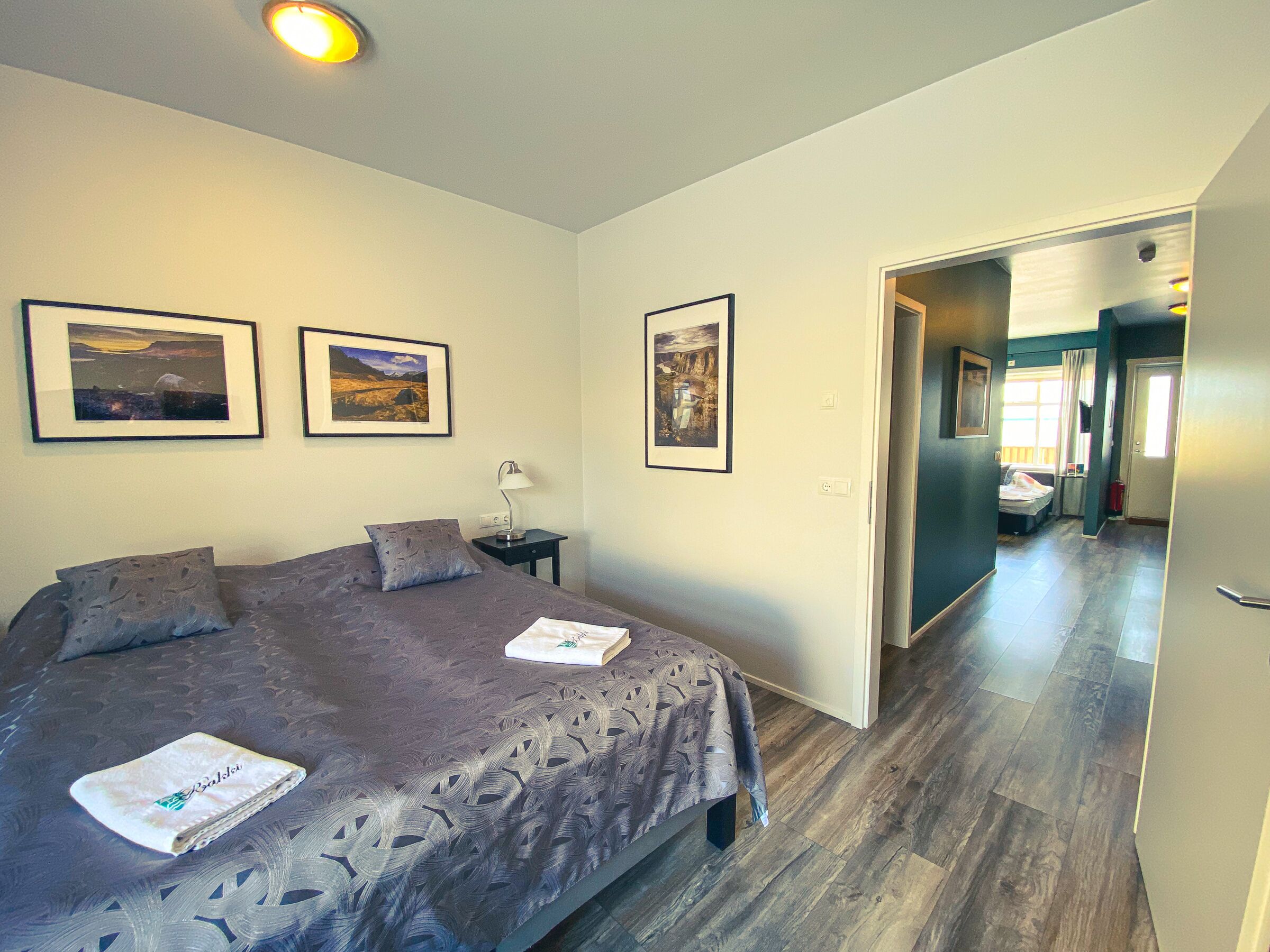 A bedroom with a large bed, a bedside table with a lamp, and three framed pictures on the wall.