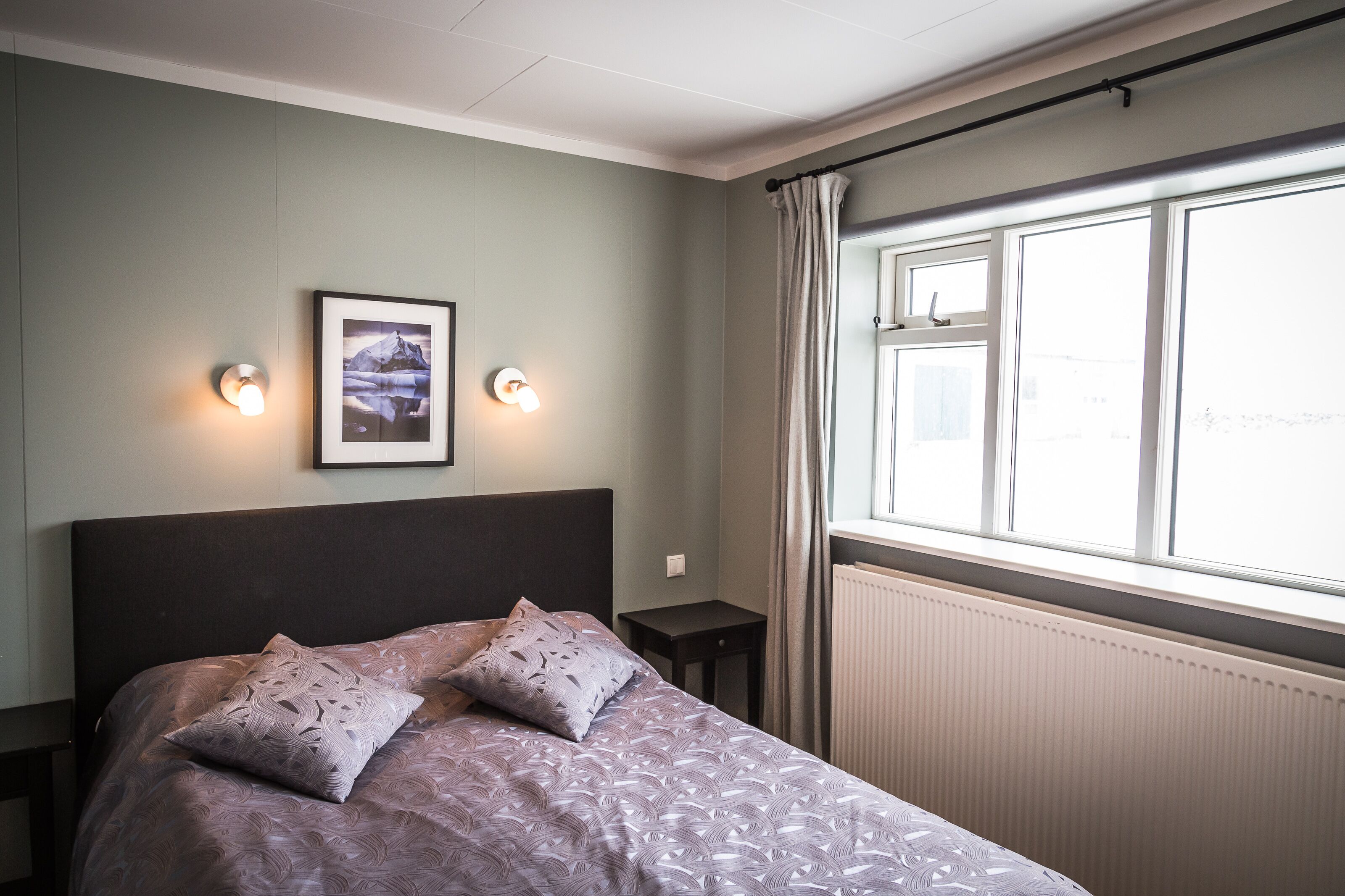 A neatly arranged bedroom with a bed, two bedside tables, a framed picture on the wall, and a window with curtains.