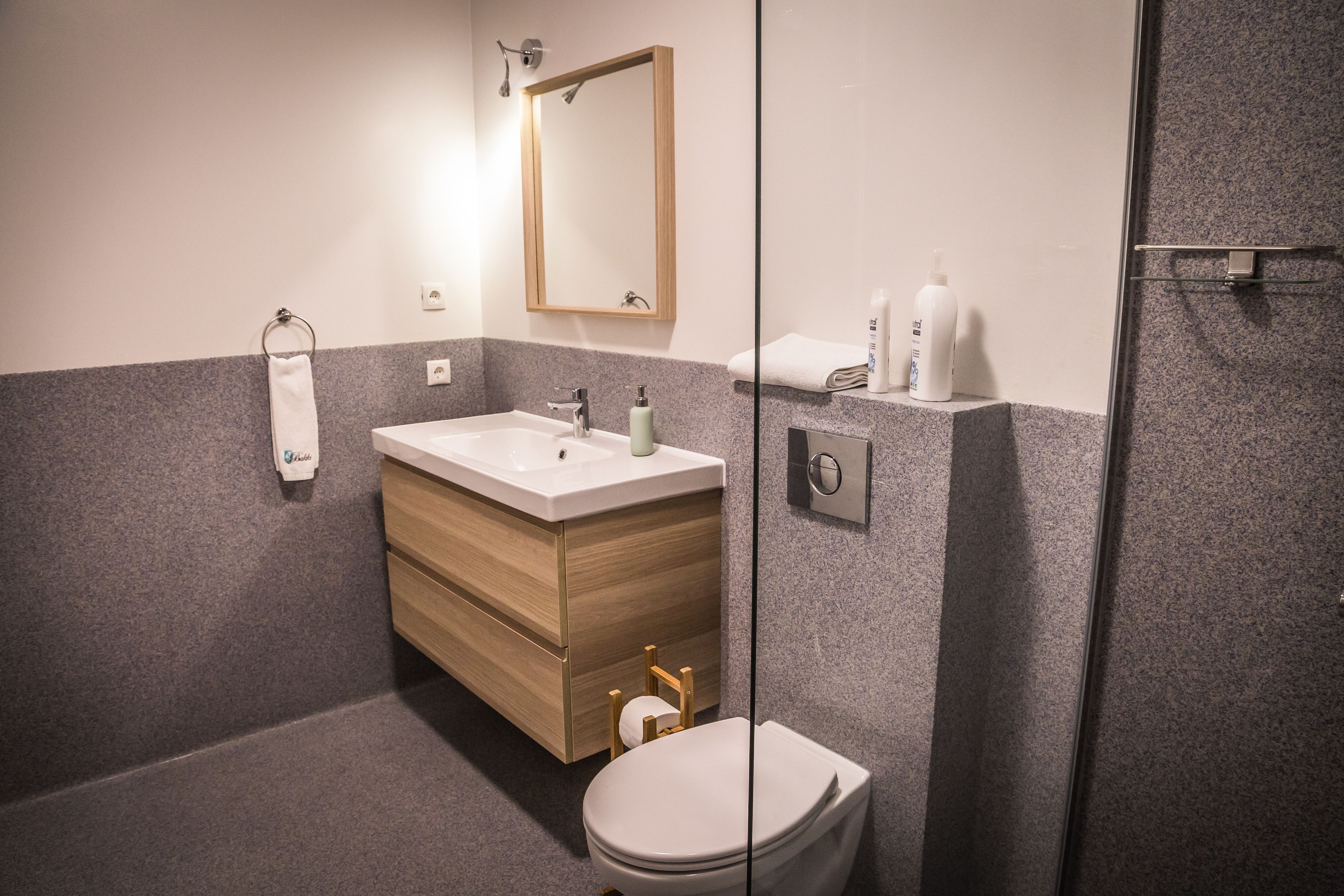 A modern bathroom with a wooden vanity, a white sink, a toilet, and a glass shower enclosure.