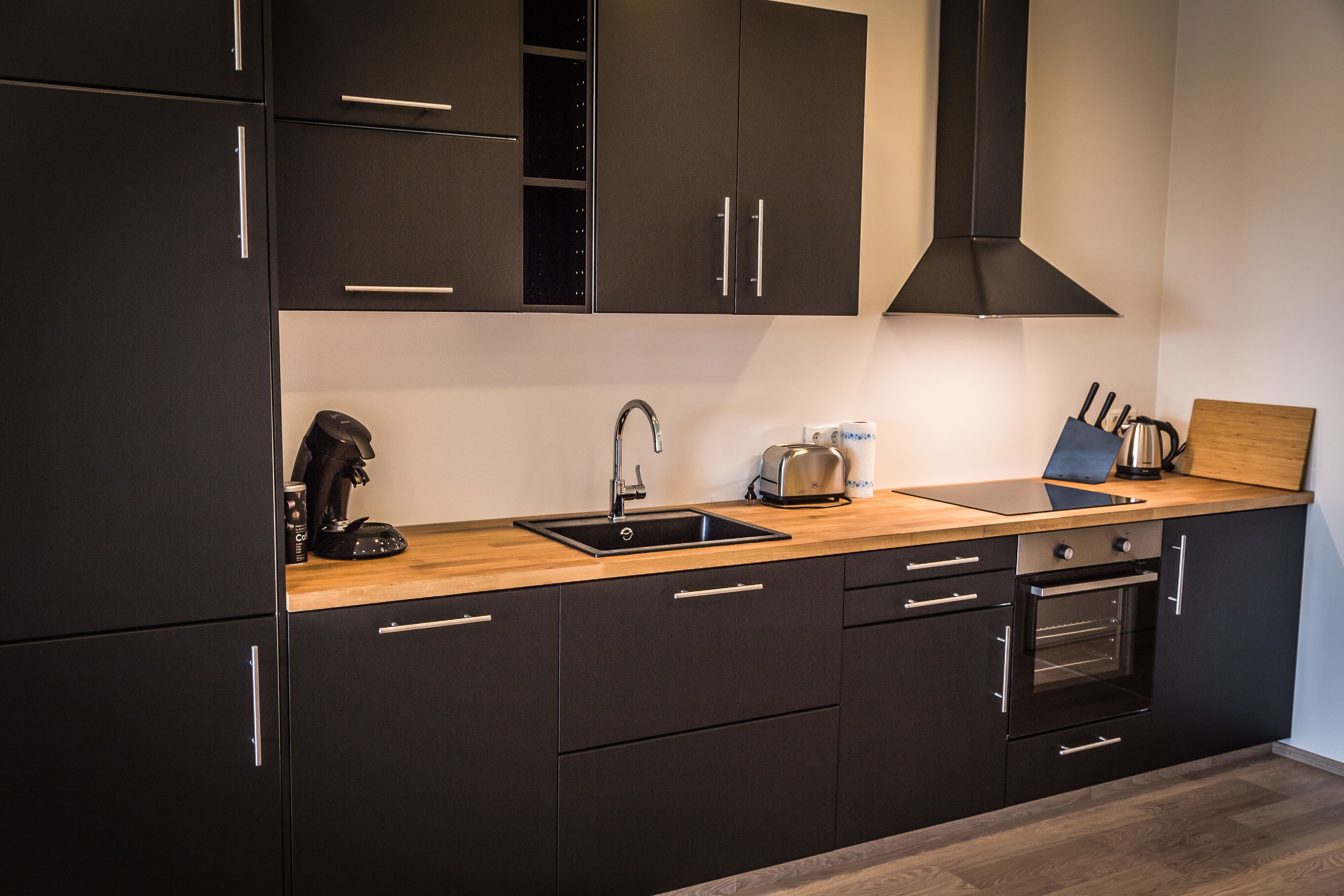 Une cuisine moderne avec des meubles de couleur noire, un plan de travail en bois, un évier, un grille-pain et un four.
