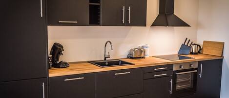 Une cuisine moderne avec des meubles de couleur noire, un plan de travail en bois, un évier, un grille-pain et un four.