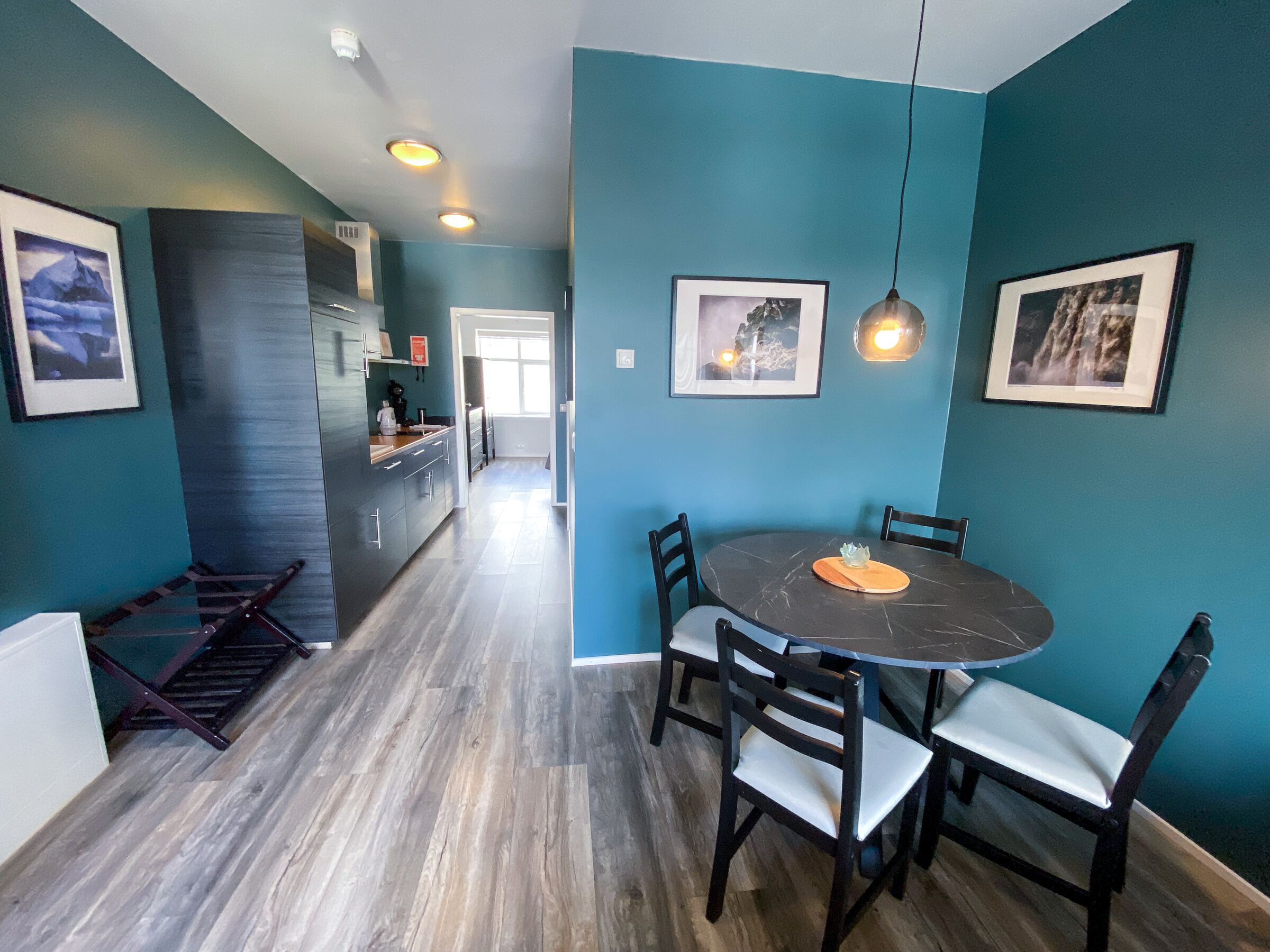 Una cocina moderna con armarios oscuros, un comedor con una mesa redonda y sillas, y paredes color turquesa.