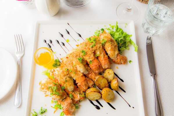 A white plate with breaded fish, potatoes, and greens, accompanied by a fork and knife on a white tablecloth. - Bakki Hostel and Apartments (Eyrarbakki)