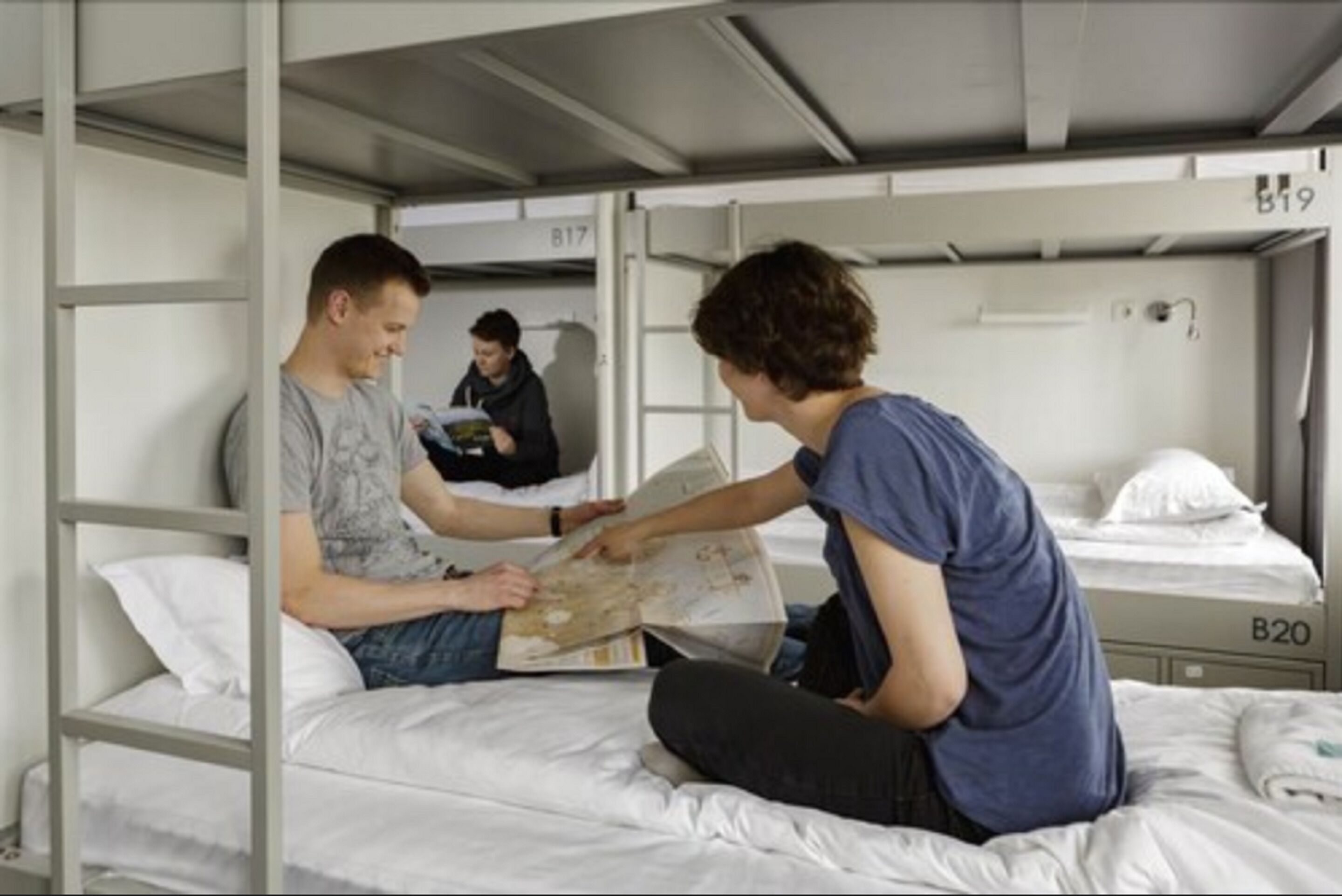 Une chambre avec un lit superposé où deux personnes sont assises sur le lit du bas, dont l’une est en train de lire un livre.