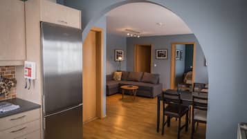 A compact kitchen with a built-in refrigerator, wooden cabinets, and a small countertop. There is a dining area with a table and chairs, and a living room with a sofa and a small round table.