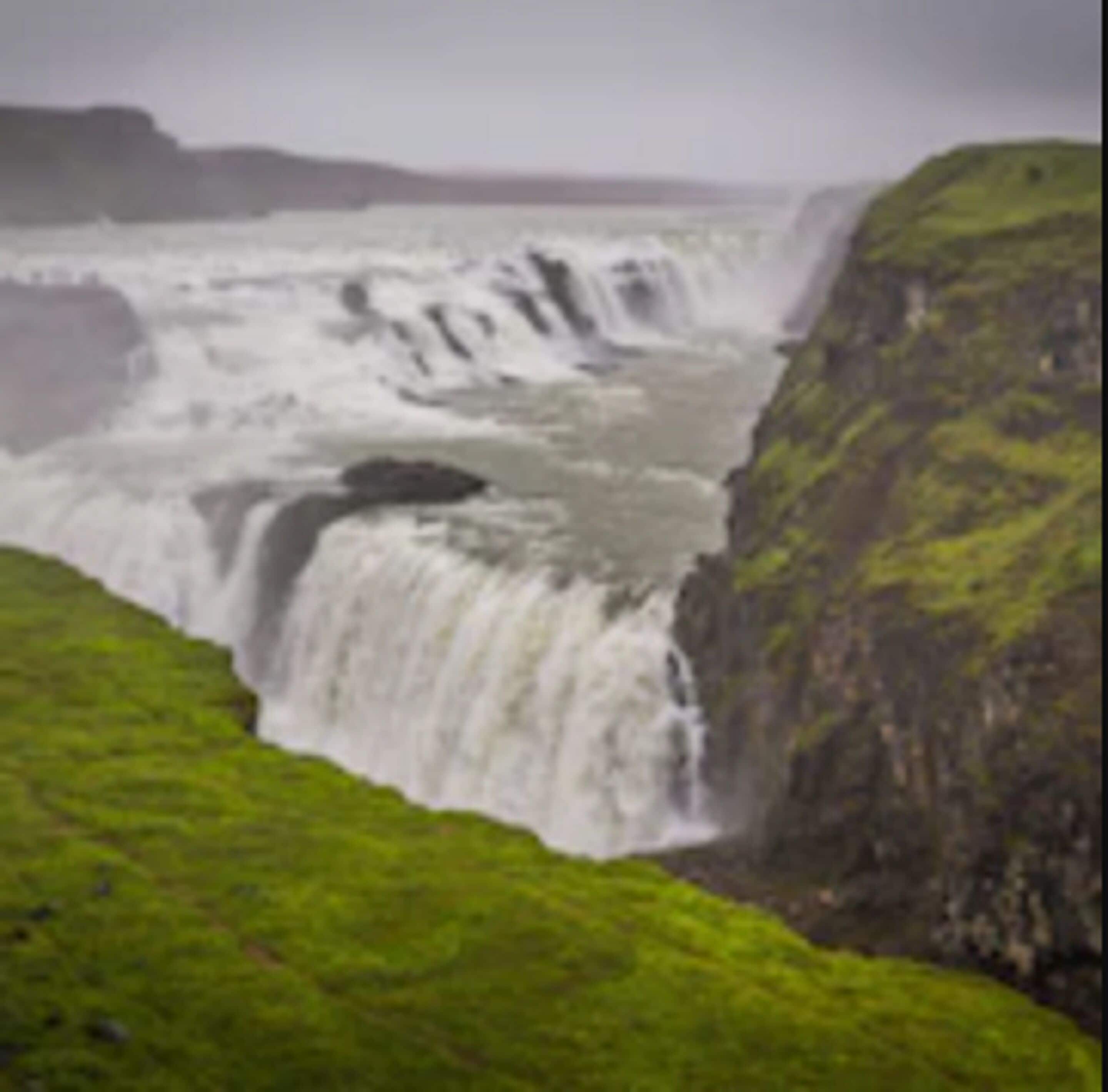 A waterfall cascading down a rocky cliff with lush green vegetation at the base.