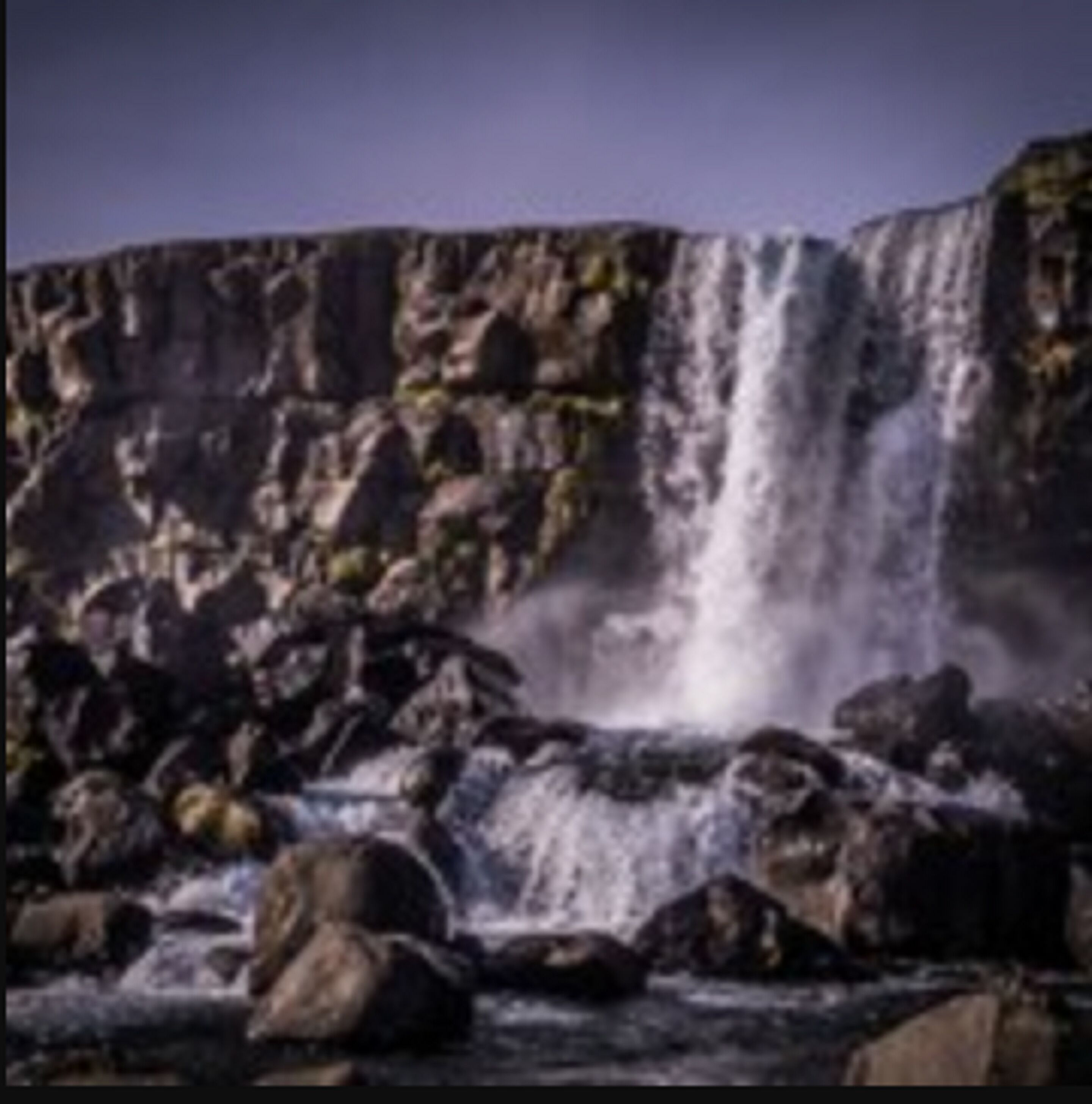 A waterfall cascading over rocks with a clear sky above.
