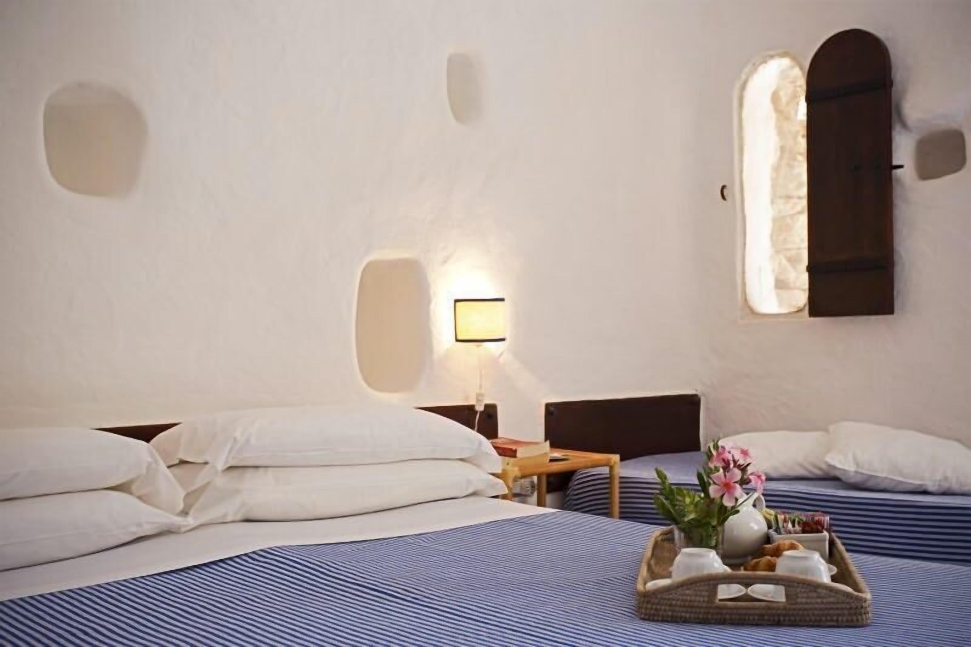 A hotel room with two beds, a nightstand, a lamp, and a tray with breakfast items.