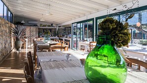 A restaurant with wooden tables and chairs, a large green vase with flowers, and a stone wall. - Albergo I Dammusi Di Borgo Cala Creta (Lampedusa)