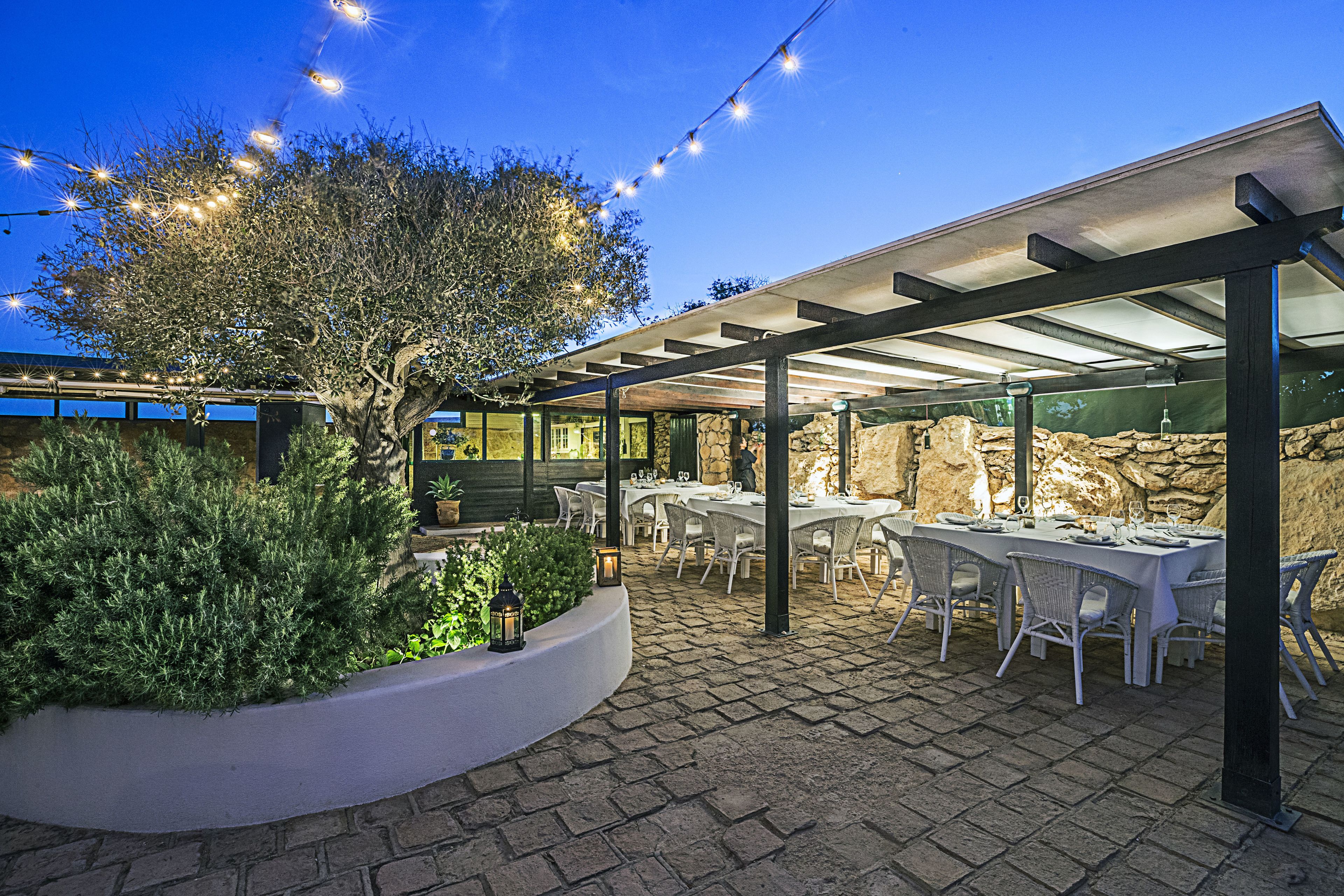 An outdoor patio with tables and chairs, string lights, and a tree.