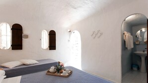 A bedroom with a bed, a bedside table with a tray of tea and flowers, and a bathroom with a sink and mirror. - Albergo I Dammusi Di Borgo Cala Creta (Lampedusa)