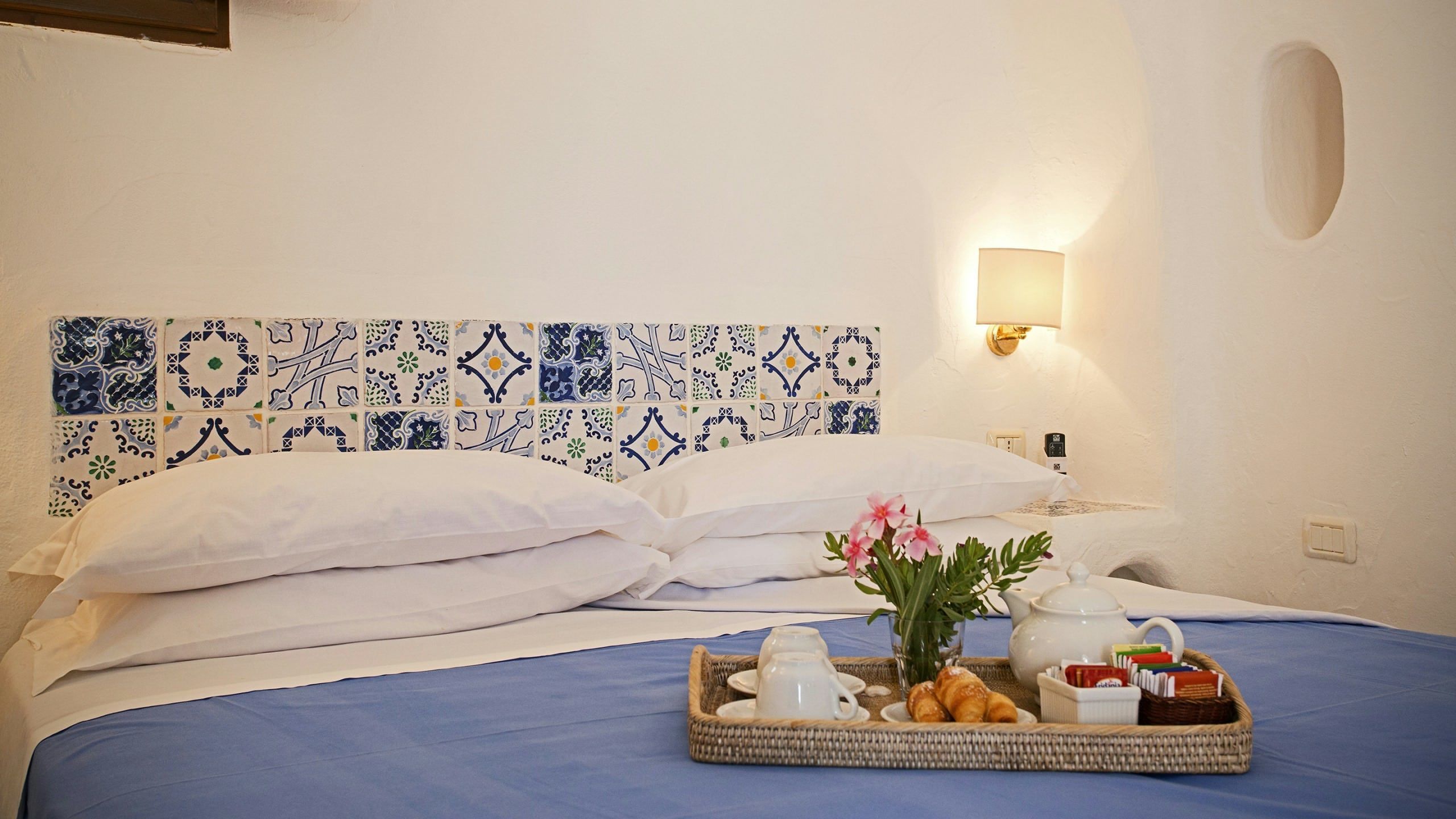A neatly made bed with a blue bedspread, white pillows, and a tray with breakfast items.