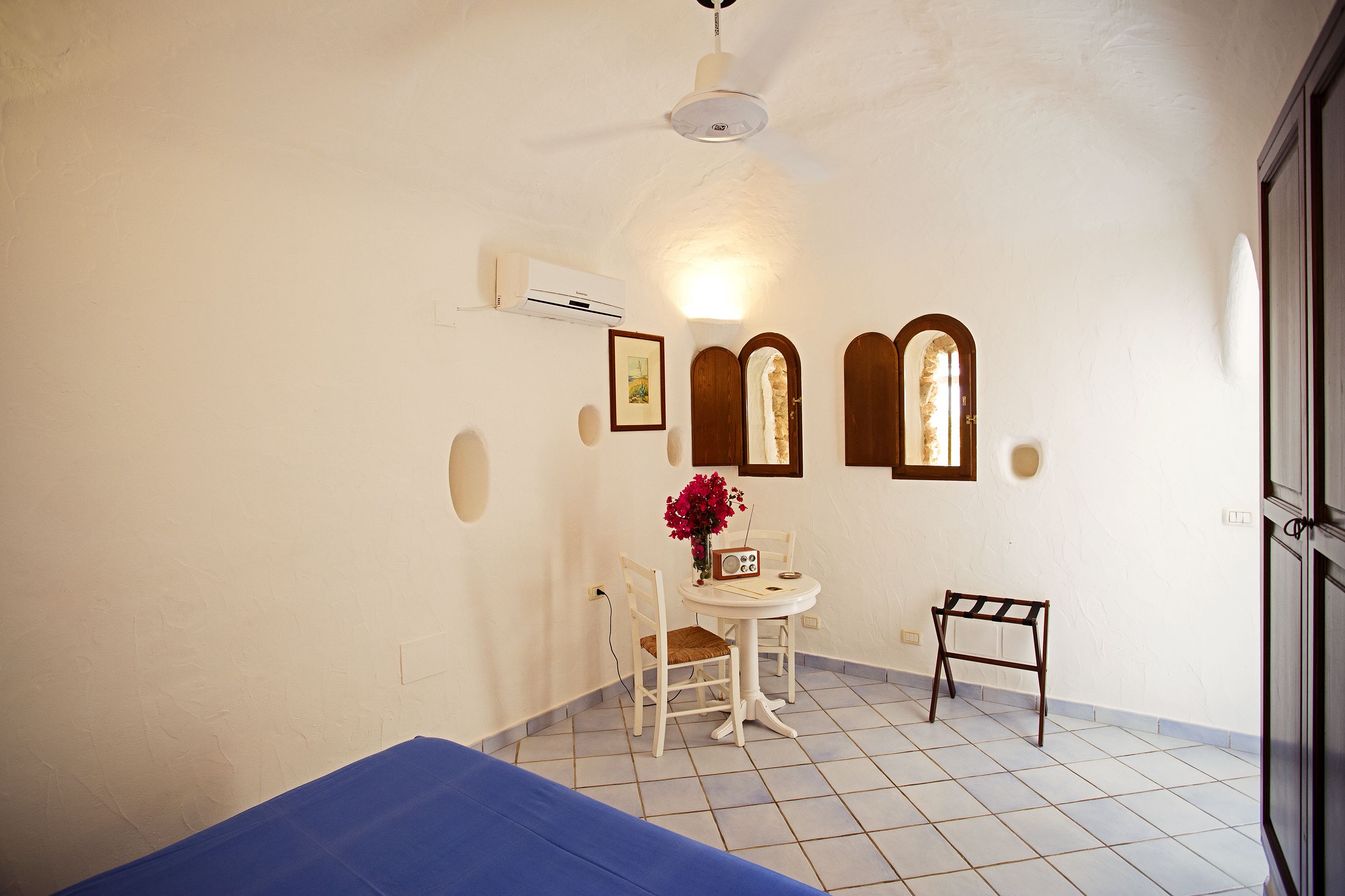 A small room with a bed, a table with a radio, and a chair.