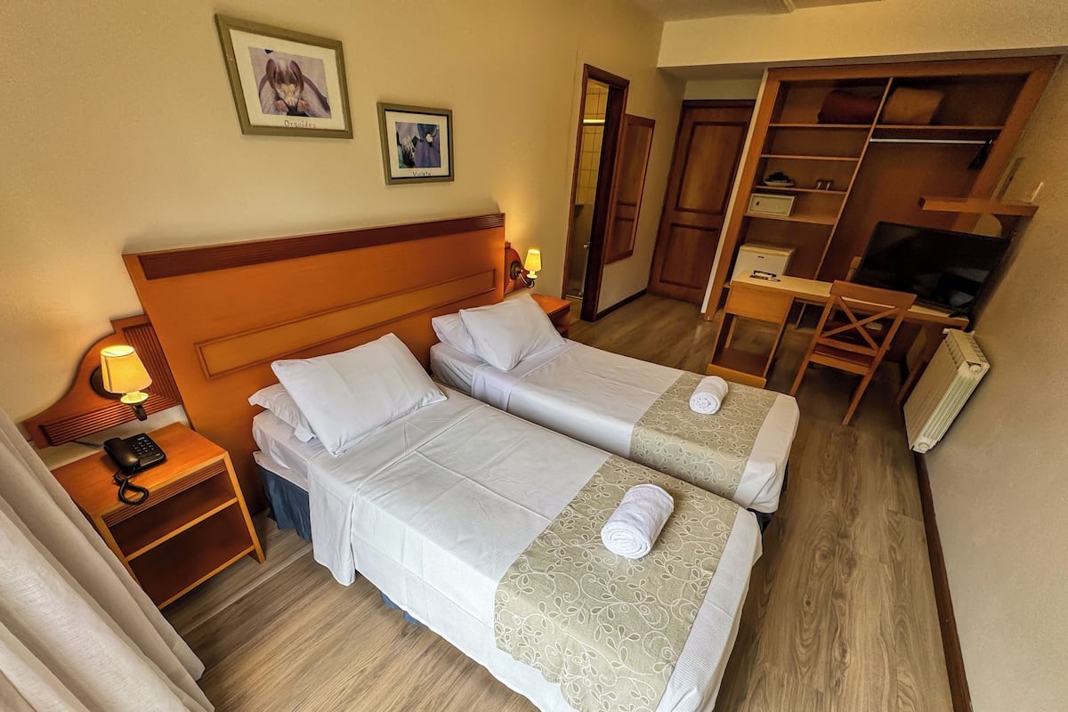 A hotel room with two beds, a desk, a chair, a wardrobe, and a nightstand with a lamp and phone.