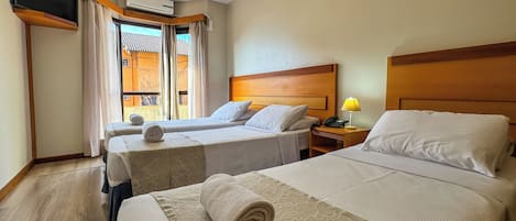 A hotel room with two beds, a TV, an air conditioner, and a window with curtains.