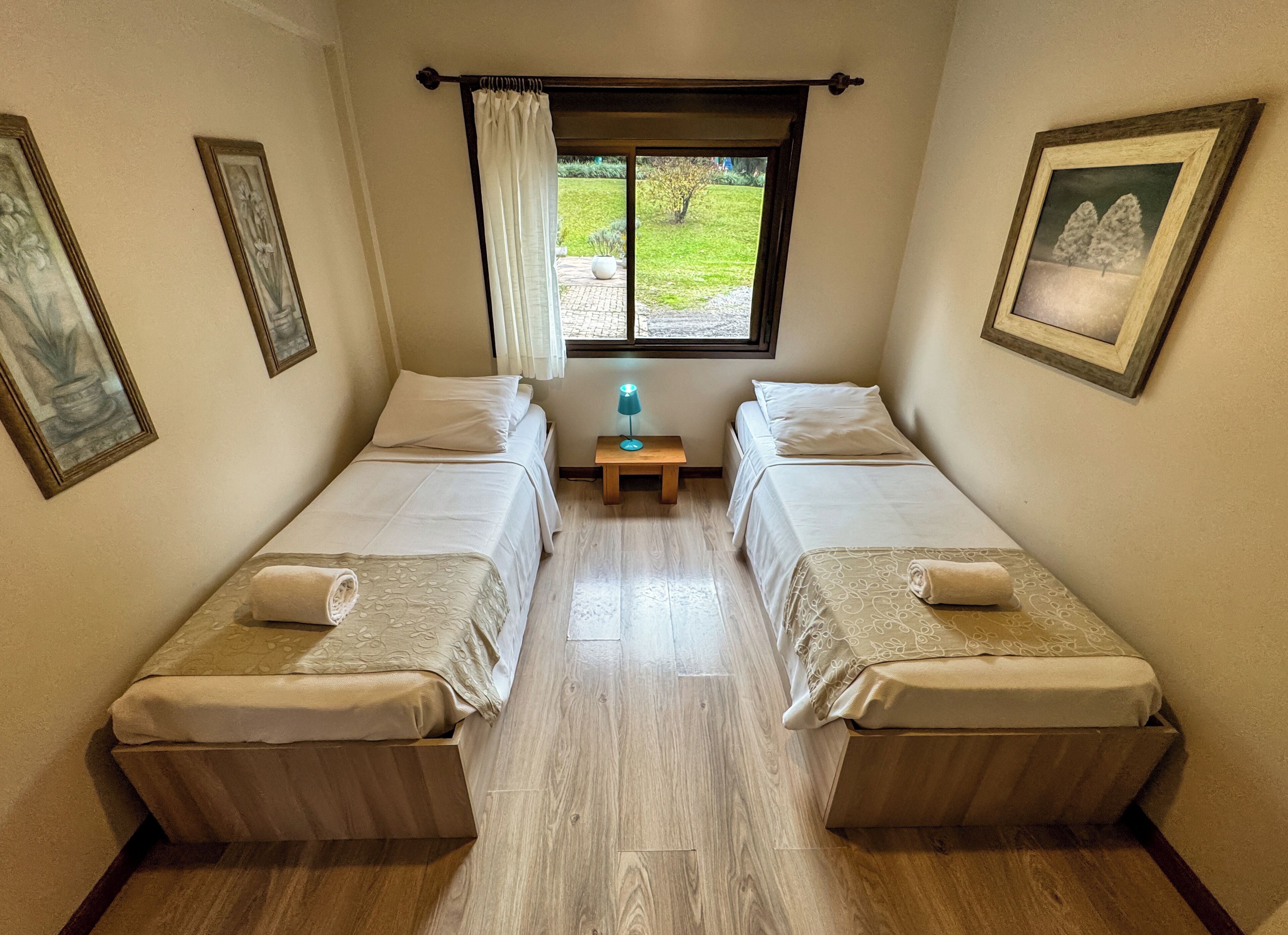 Une chambre avec deux lits simples, une table de chevet avec une lampe et une fenêtre donnant sur un jardin.