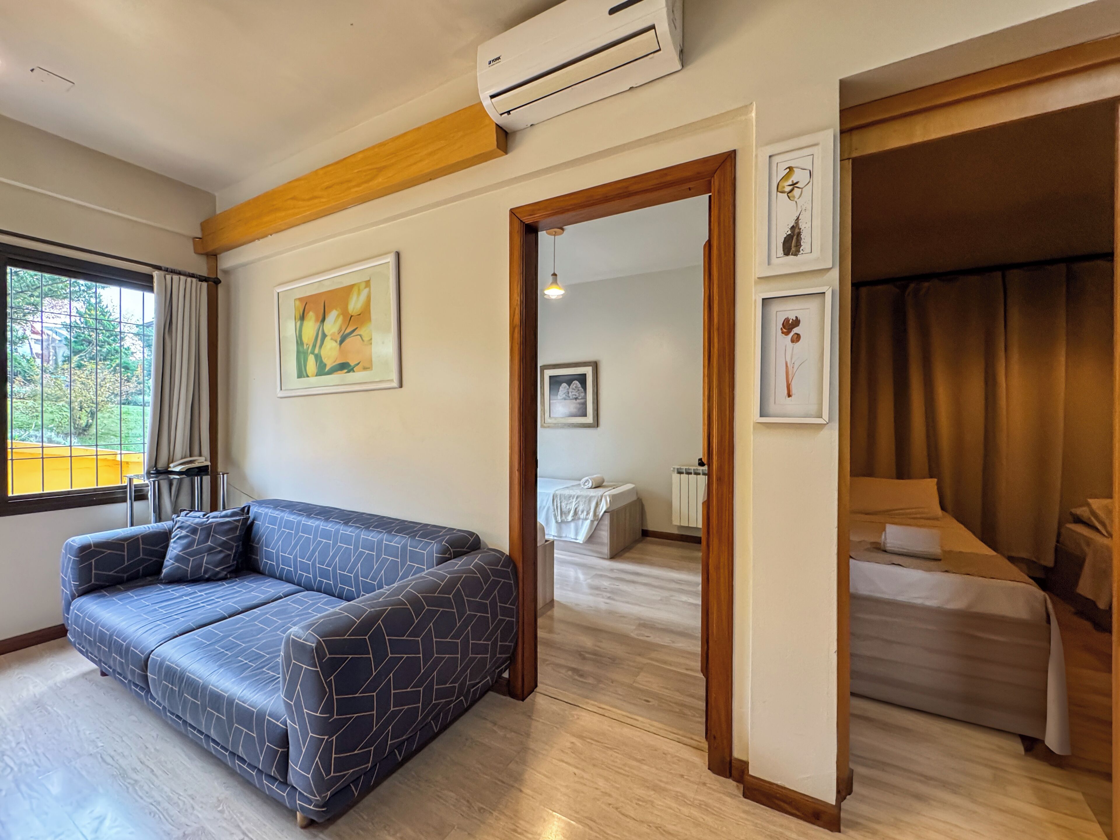 A modern hotel room with a sofa, a bed, a dining area, and a view of greenery outside.