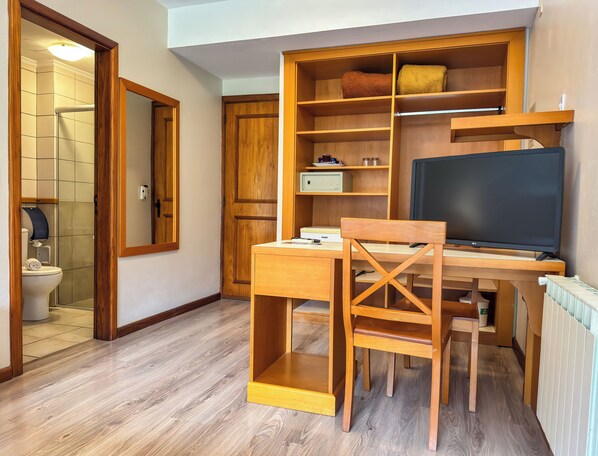 A compact room with a wooden desk, a chair, a television, and a built-in shelving unit.