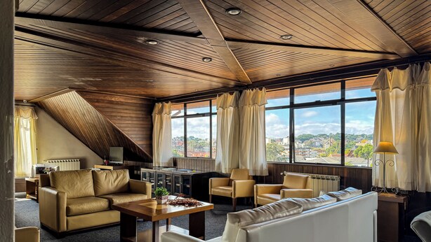 Una sala de estar moderna con techo inclinado, ventanas amplias y vista a un paisaje urbano.
