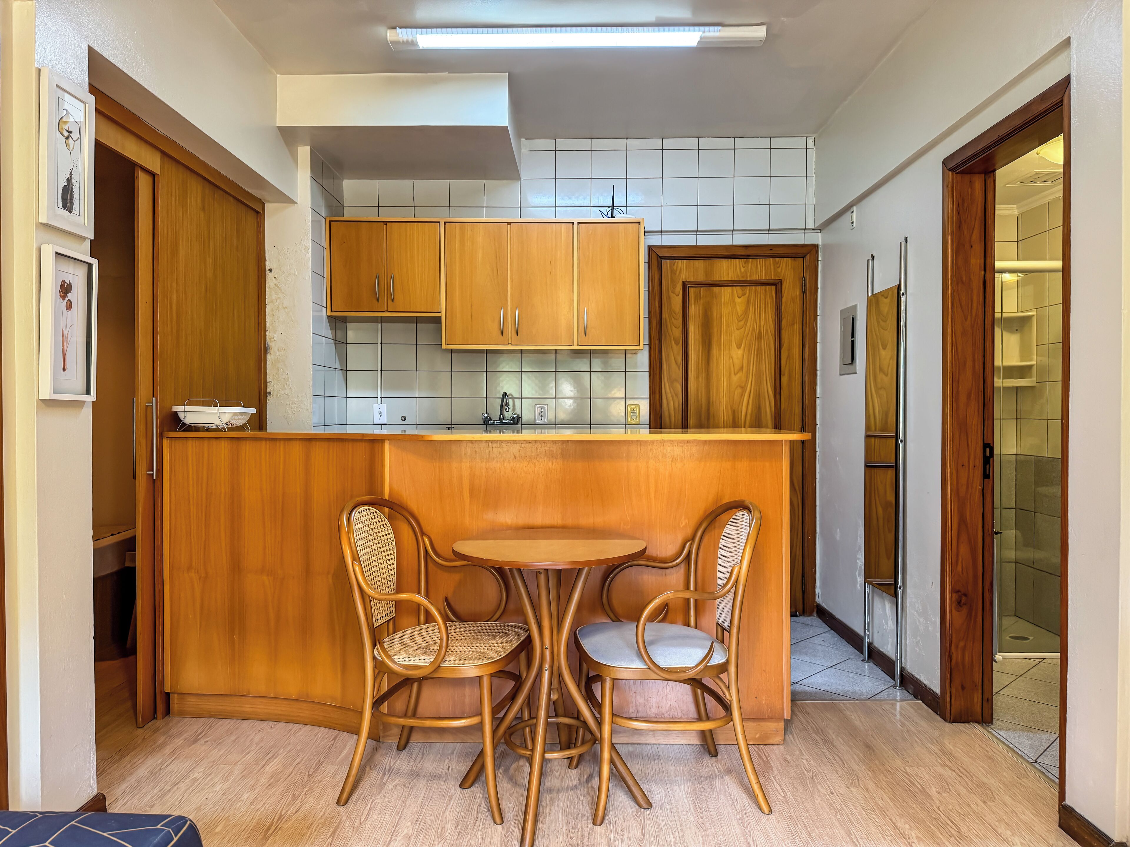 Cocina compacta con armarios de madera, una pequeña mesa de comedor y dos sillas de mimbre.