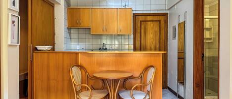 Cocina compacta con armarios de madera, una pequeña mesa de comedor y dos sillas de mimbre.