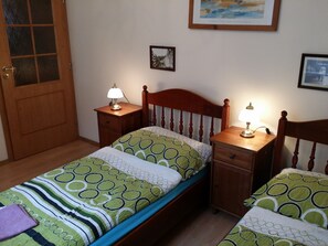Um quarto com uma cama de solteiro, duas mesas de cabeceira, uma porta de madeira e um quadro pendurado na parede.