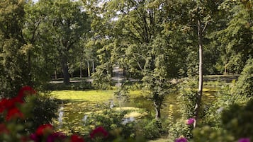 Ein friedlicher Garten mit Teich, umgeben von üppigen Bäumen und leuchtenden Blumen.