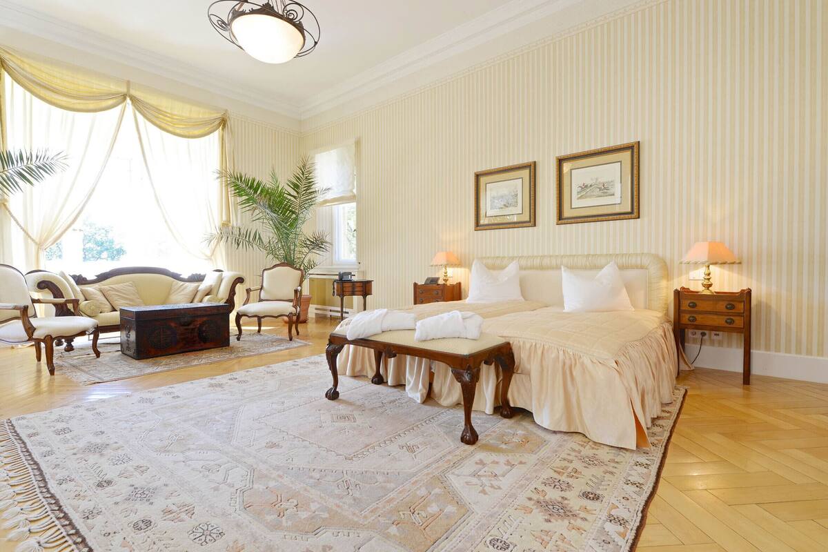 A spacious bedroom with a large bed, a sitting area with chairs, a coffee table, and a large rug.