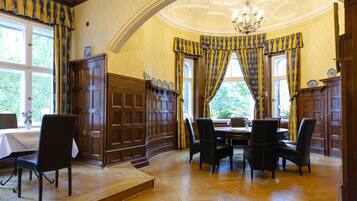 Comedor con mesa y sillas de madera, una araña y ventanas grandes con cortinas.