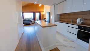A modern kitchen with a central island, white cabinetry, and a wooden accent wall. - Eden Resort Anzère (Ayent)