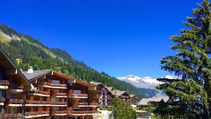 A multi-story lodge with balconies, set against a backdrop of mountains and a clear sky. - Eden Resort Anzère (Ayent)