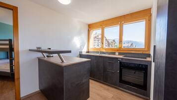 A modern kitchen with dark cabinetry, a built-in oven, and a window overlooking a mountainous landscape.