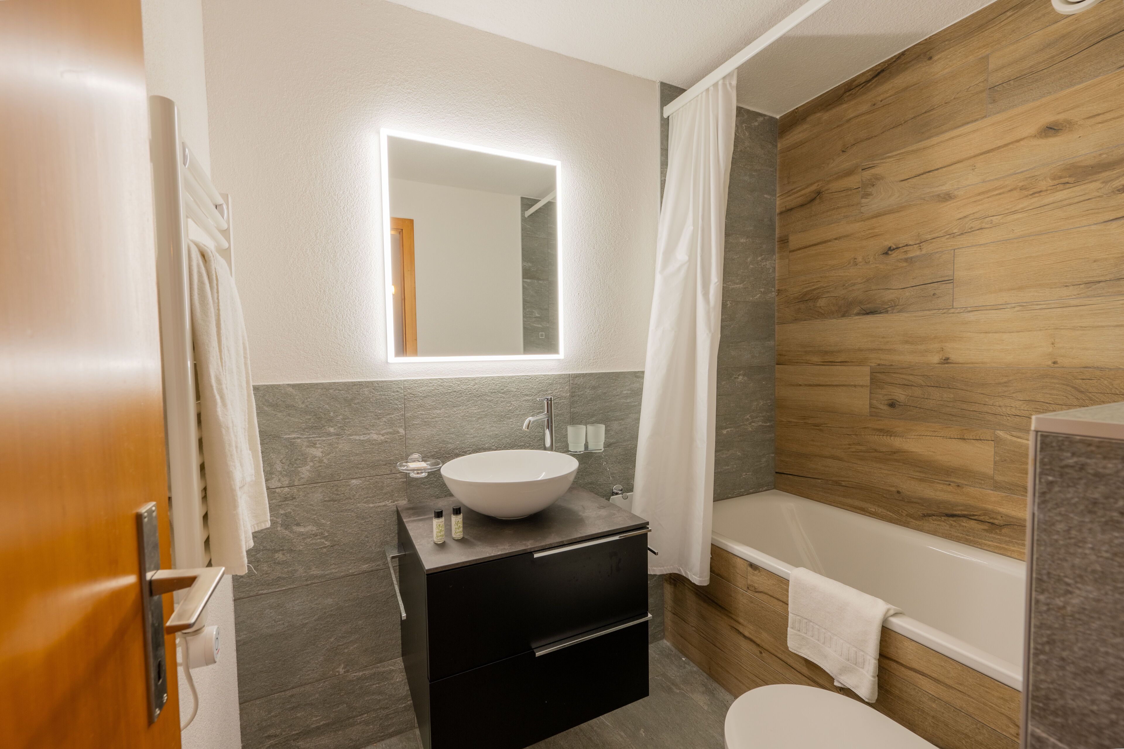 A modern bathroom with a wooden wall, a white sink, and a bathtub.