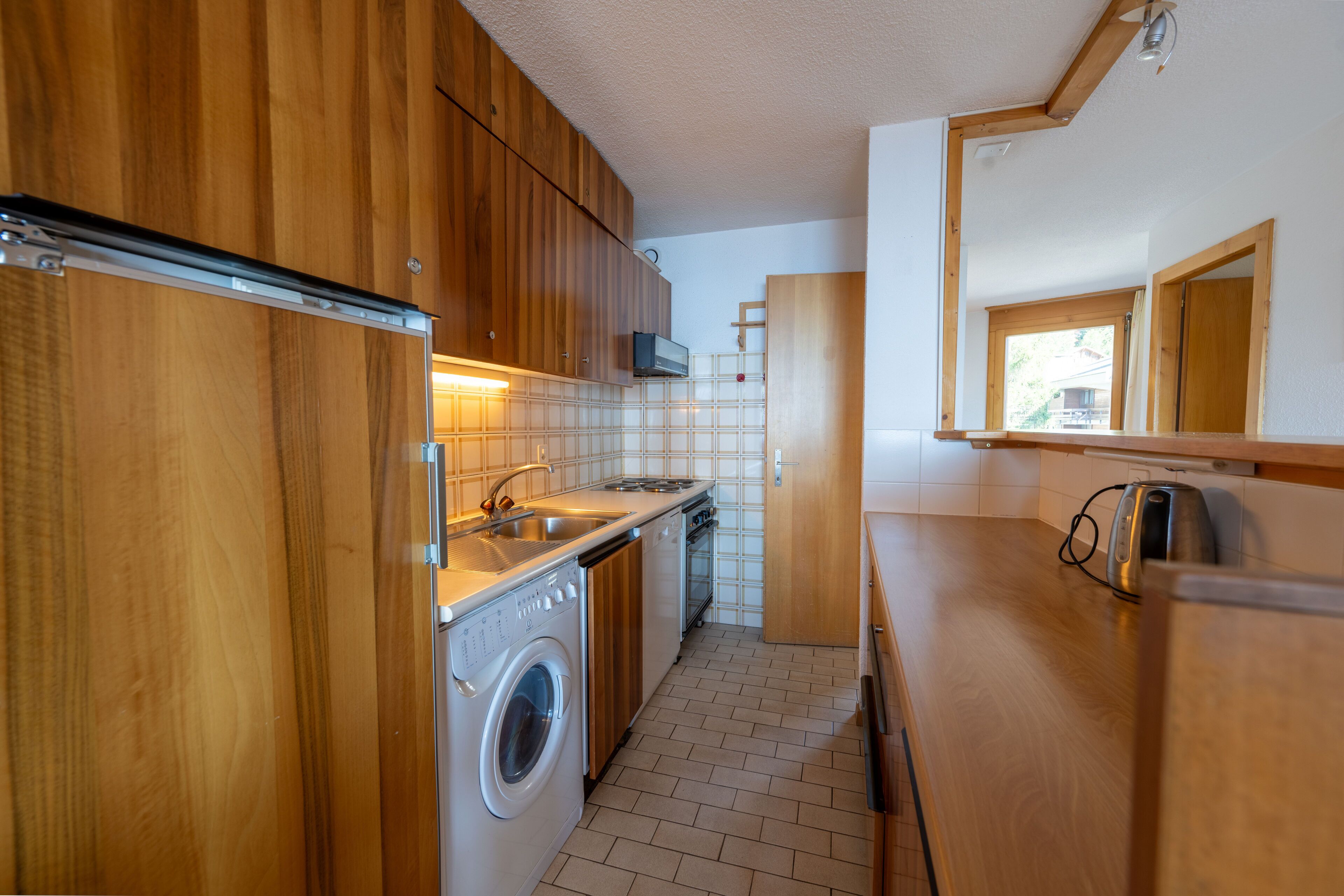 A compact kitchen with wooden cabinets, a washing machine, a built-in oven, and a toaster.