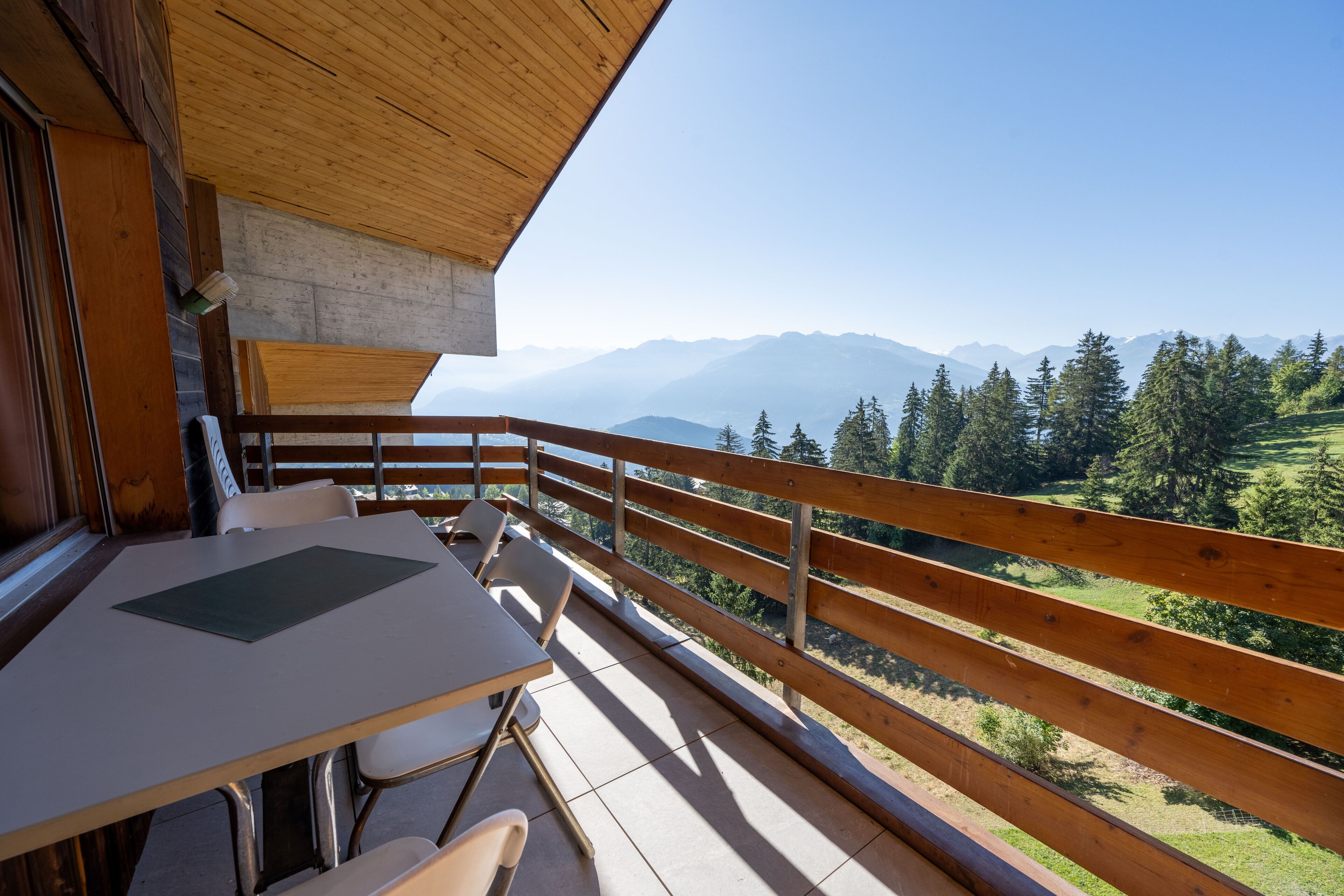 Un balcón de madera con una mesa y sillas, con vistas a un paisaje montañoso.