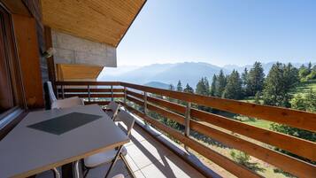 Un balcón de madera con una mesa y sillas, con vistas a un paisaje montañoso.