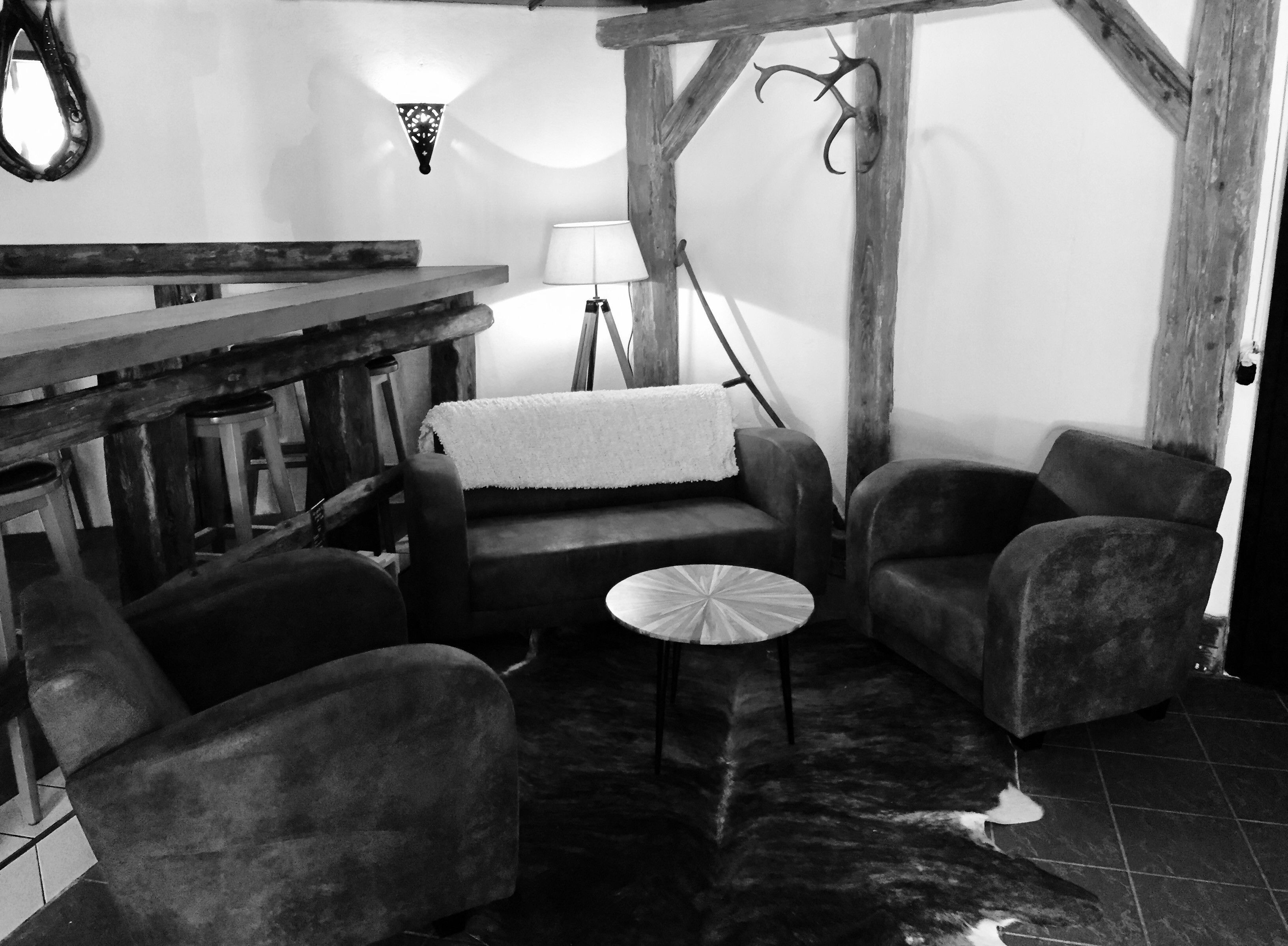 Un interior rústico con un banco de madera, dos sillones, una mesita redonda y una lámpara.