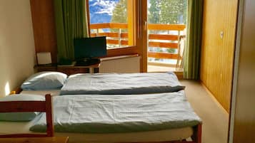 A room with two beds, a television, and a view of mountains through a large window.
