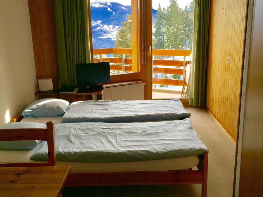 A room with two beds, a television, and a view of mountains through a large window.