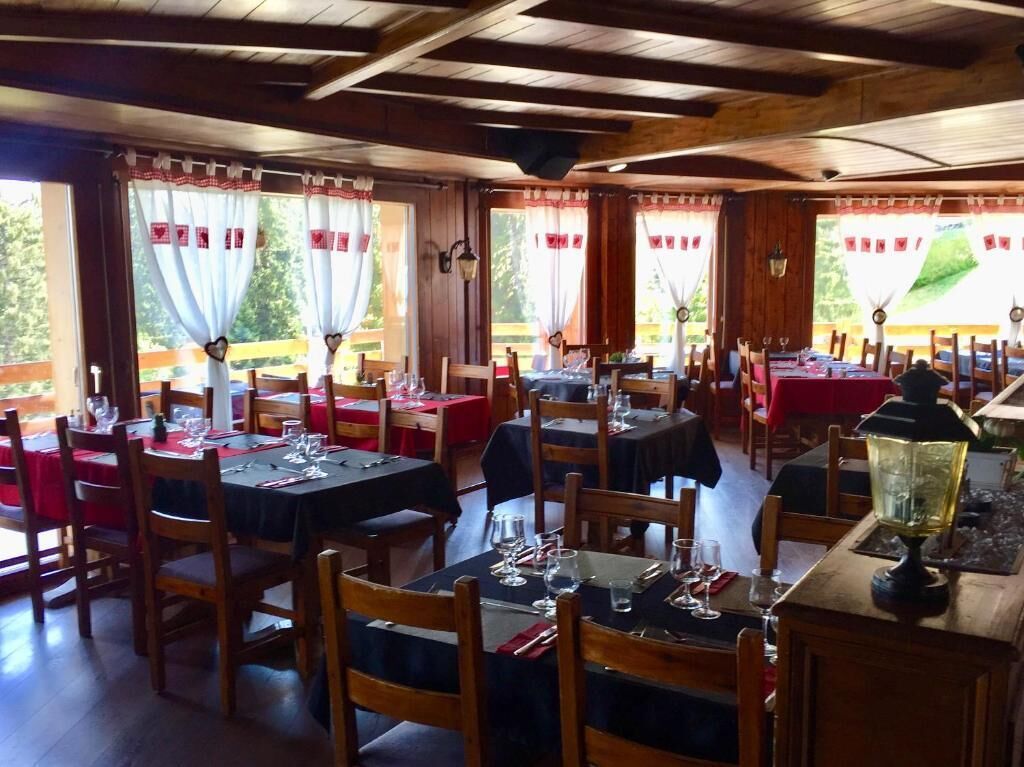 Un restaurant à l’intérieur en bois, avec des tables recouvertes de nappes rouges et une vue sur la verdure environnante.