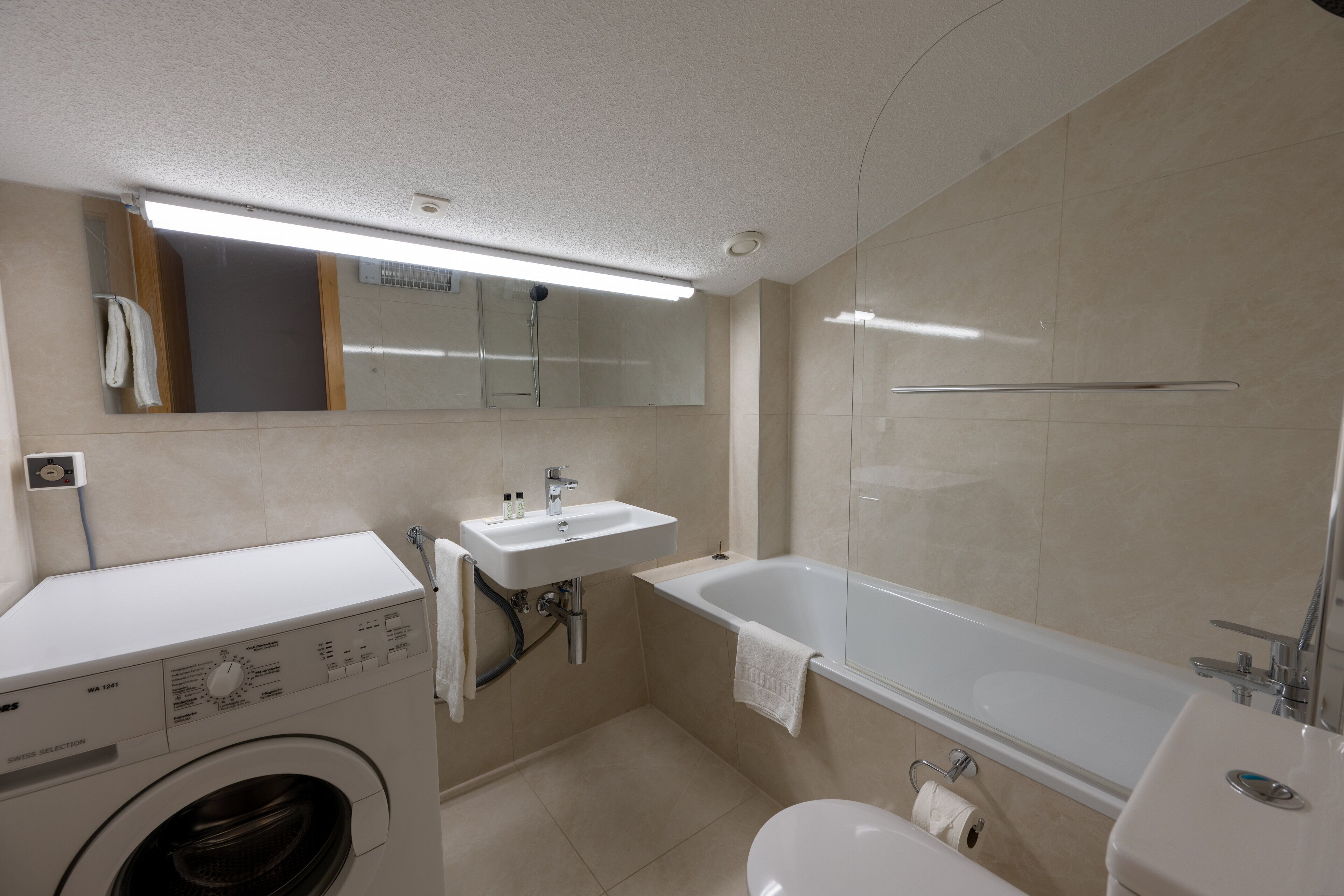 A modern bathroom with a washing machine, sink, and bathtub.
