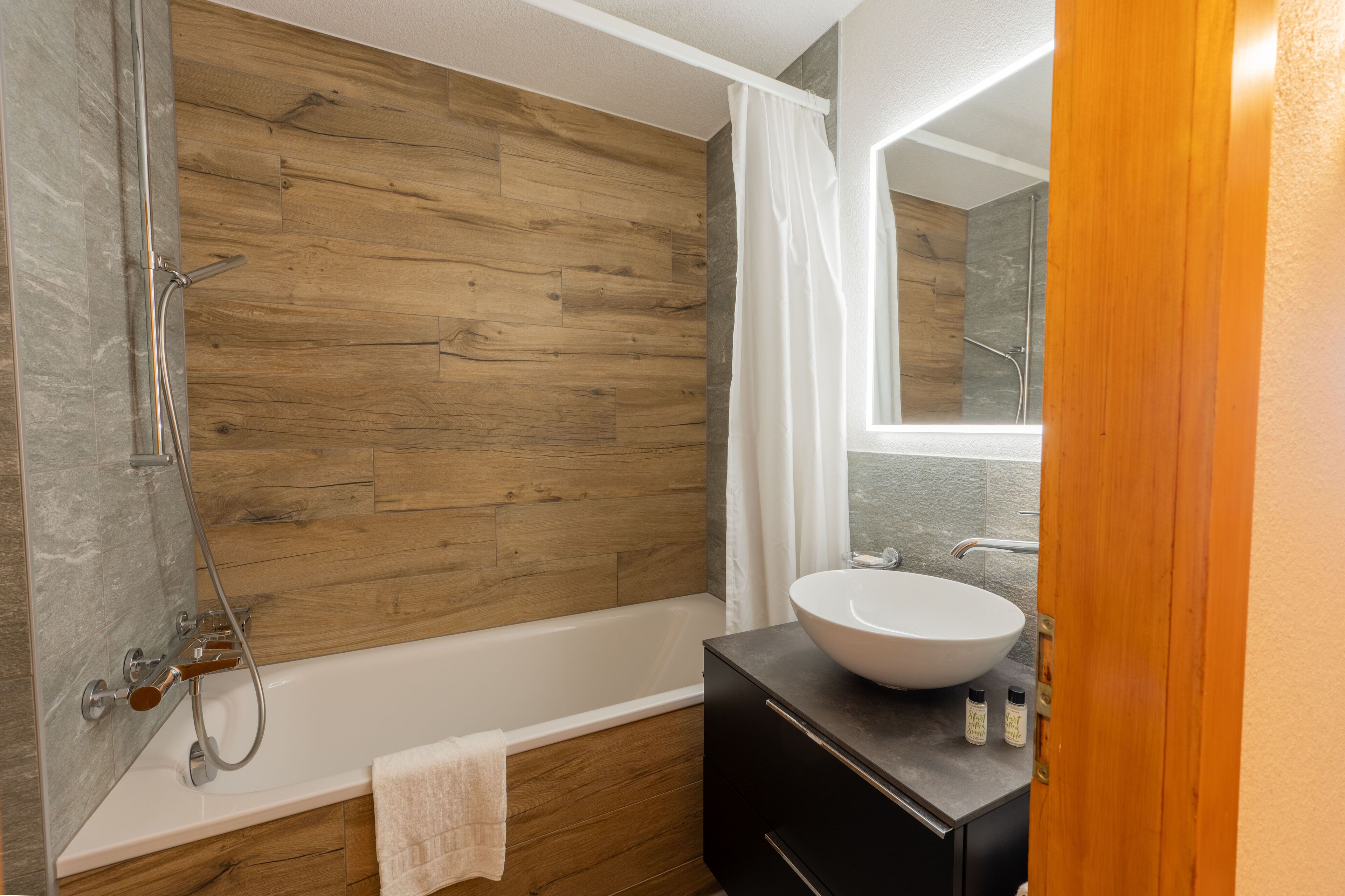 Een moderne badkamer met een houten wand, een witte badkuip, een grote wastafel en een douchehoek.